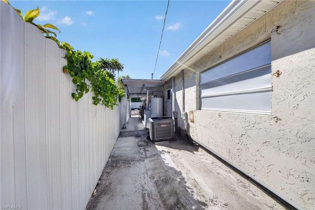 Exterior pathway featuring a white privacy fence, stucco siding, and a window with horizontal louvered panels