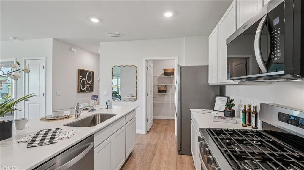 Modern kitchen featuring white cabinetry, light-toned countertops, wood-finish flooring, stainless steel appliances, and an integrated sink with a gooseneck faucet