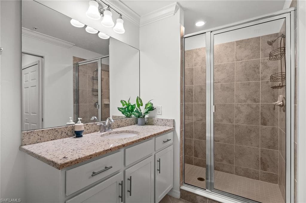 Bathroom featuring a spacious walk-in shower with tile surround, a single vanity with stone countertop, and a large mirror