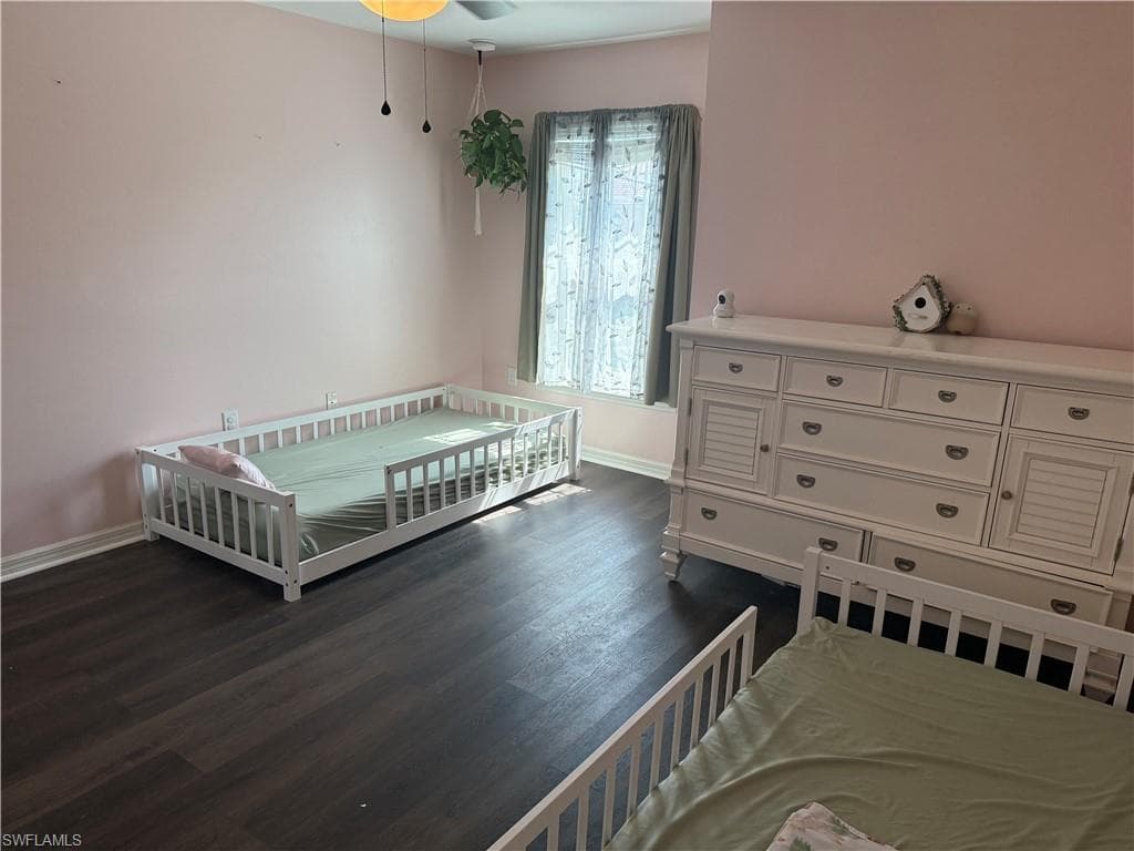 Room featuring dark wood-finish flooring, light-toned walls, and a window with sheer and solid curtains