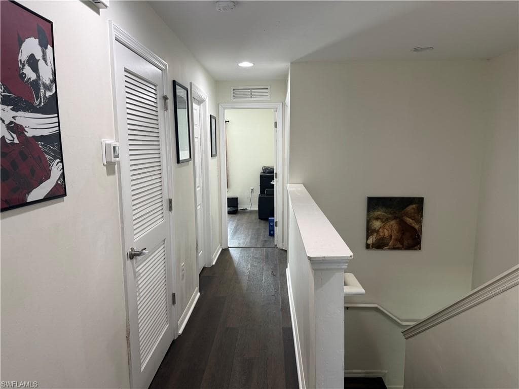 Hallway featuring wood-finish flooring, white paneled doors with louvered sections, recessed lighting, and a white staircase with a matching railing