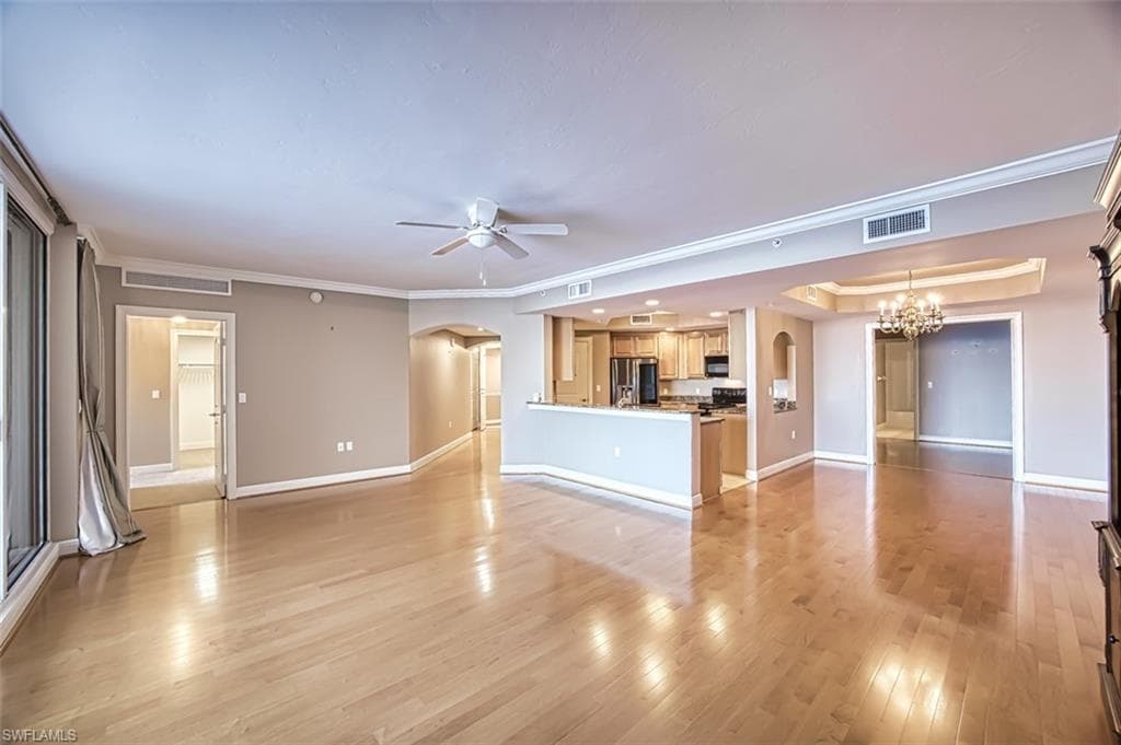 Unfurnished living room with ceiling fan with notable chandelier, light hardwood / wood-style floors, ornamental molding, and a tray ceiling