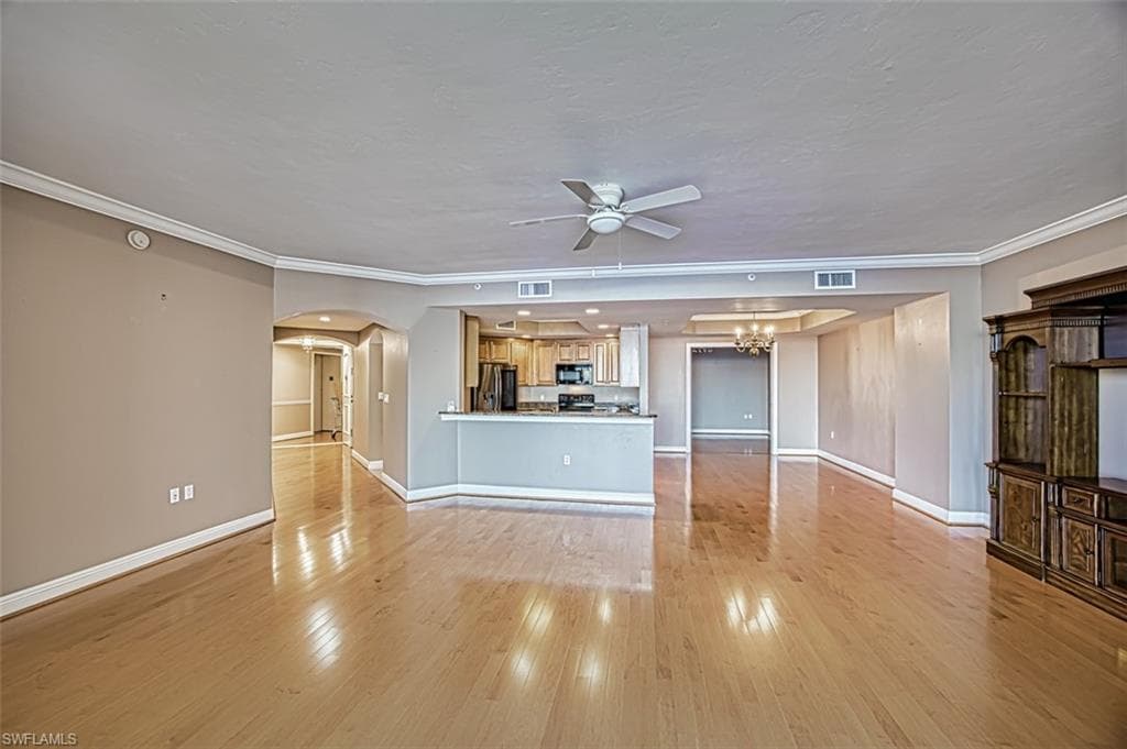 Unfurnished living room with ceiling fan with notable chandelier, light hardwood / wood-style flooring, and crown molding