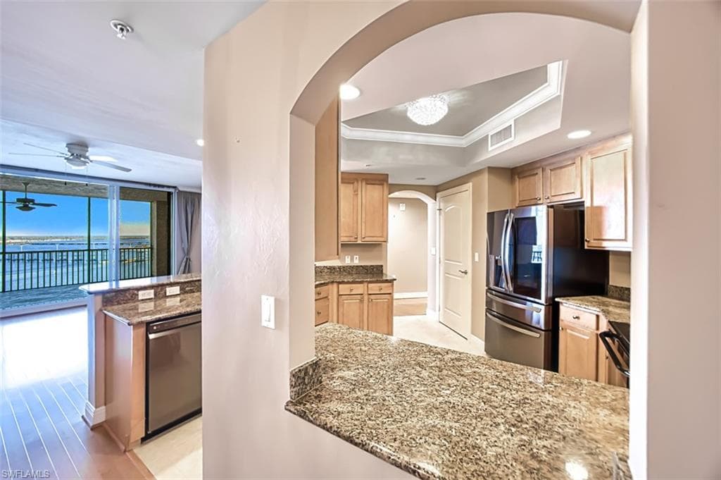 Kitchen with light stone countertops, light brown cabinetry, stainless steel appliances, a raised ceiling, and crown molding