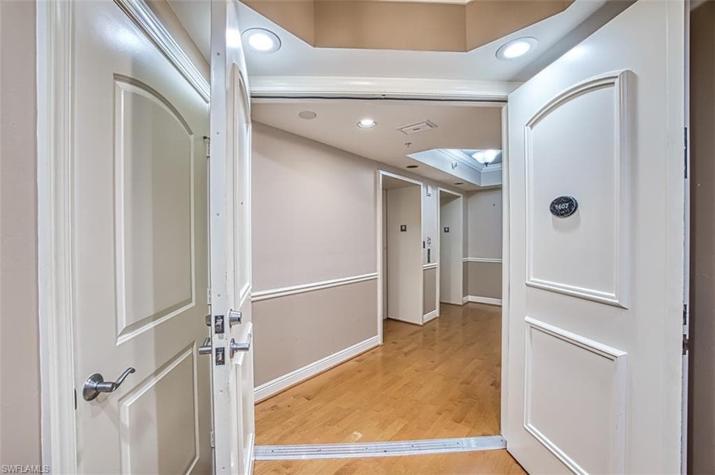 Hallway with hardwood / wood-style floors, a raised ceiling, and crown molding