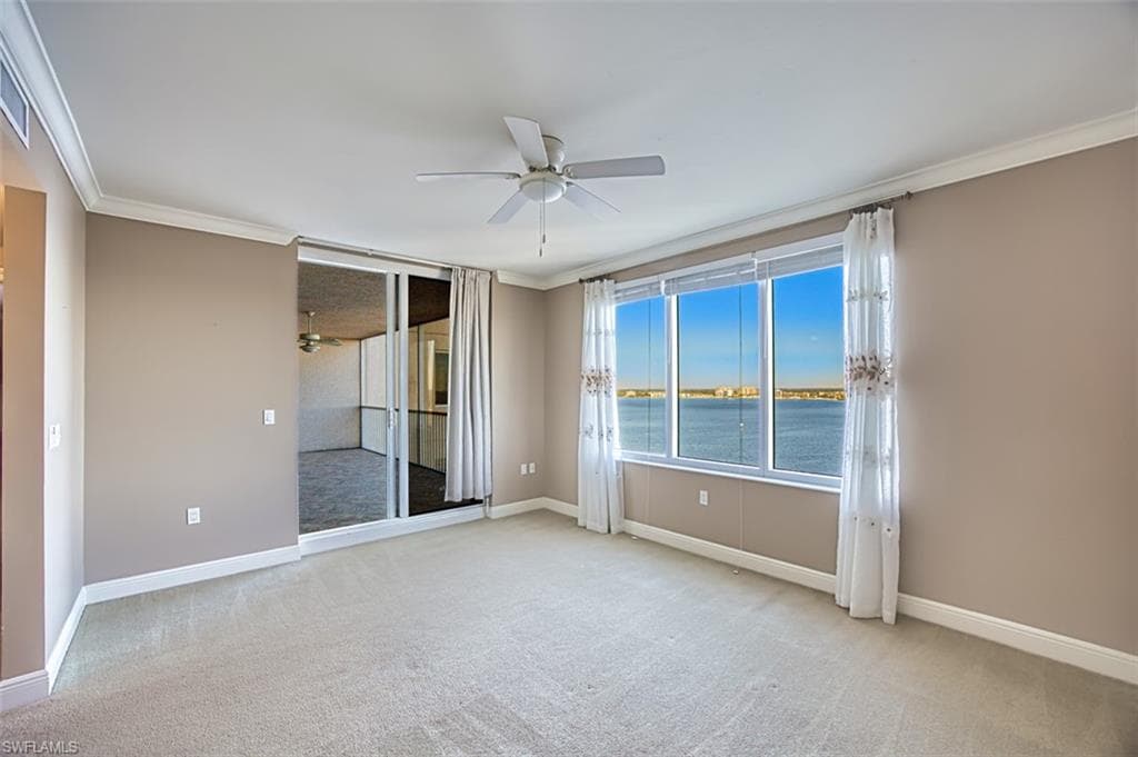 Empty room featuring light carpet, crown molding, a water view, and ceiling fan