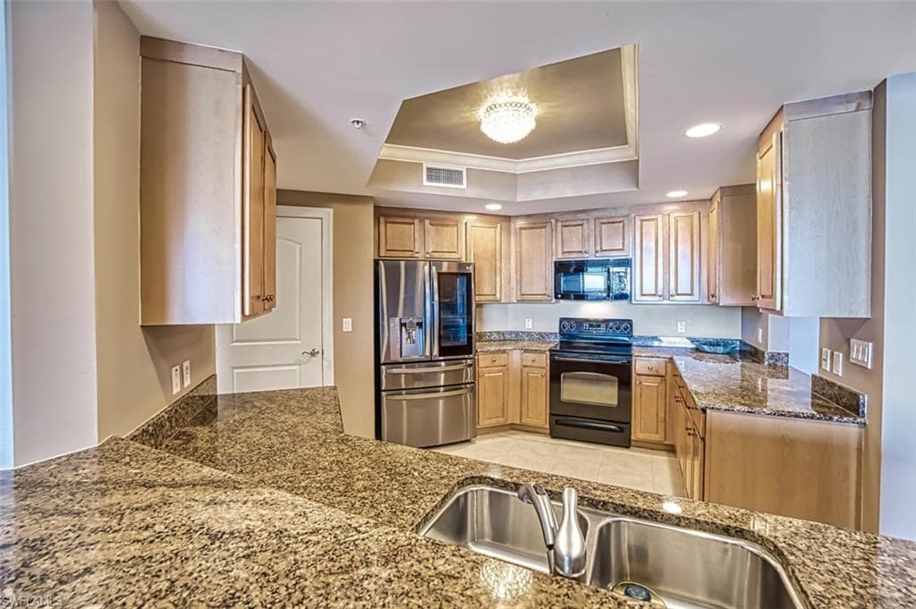Kitchen with a tray ceiling, dark stone countertops, sink, and black appliances
