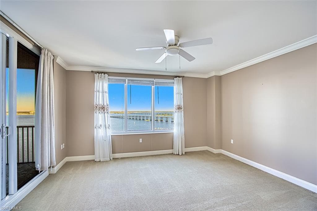 Carpeted spare room with a water view, ceiling fan, and crown molding