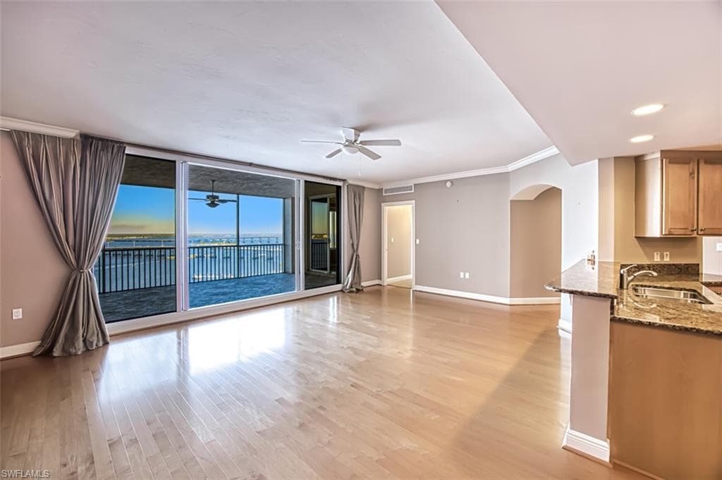 Unfurnished living room with floor to ceiling windows, ceiling fan, sink, light hardwood / wood-style floors, and ornamental molding
