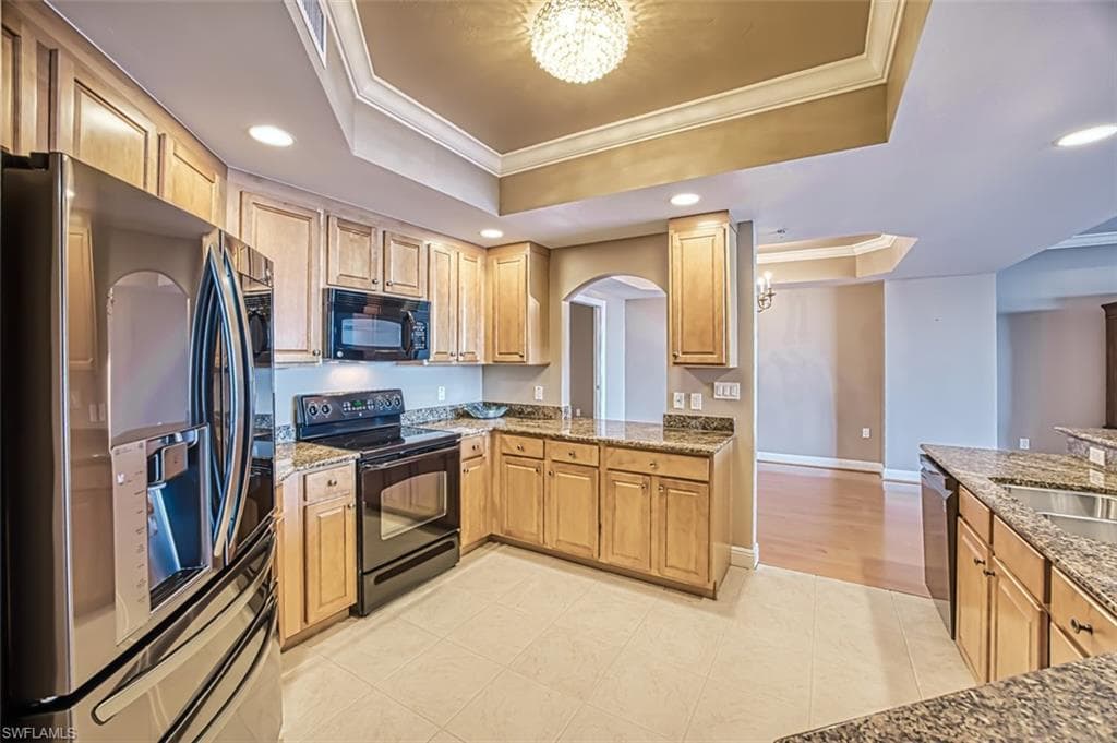 Kitchen with black appliances, a notable chandelier, a raised ceiling, and crown molding