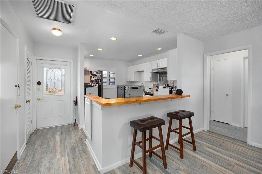 Kitchen with wooden counters, a peninsula, a breakfast bar area, white cabinets, and recessed lighting