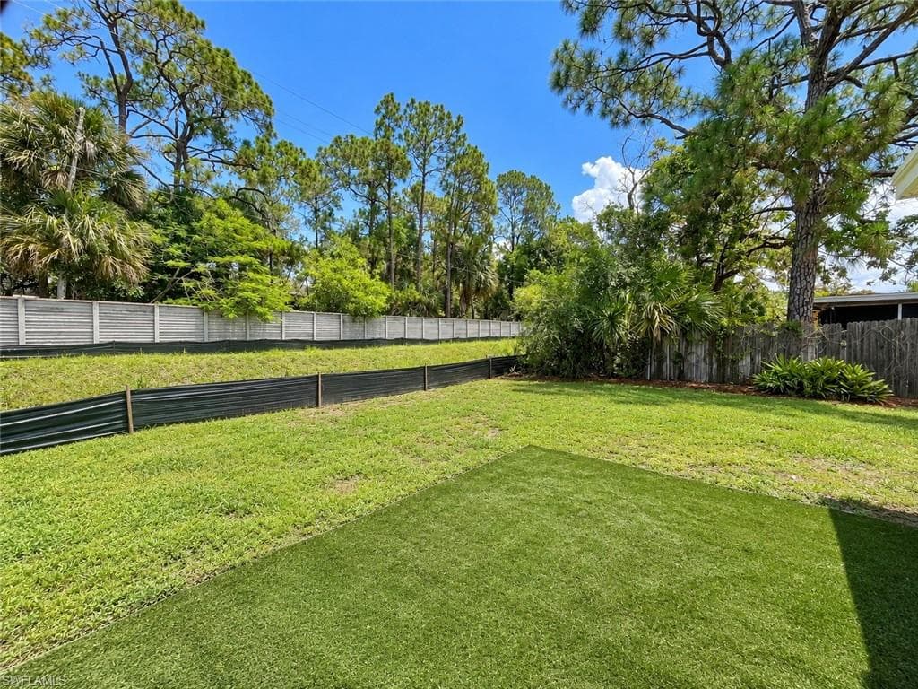 Expansive backyard featuring a combination of natural grass and artificial turf, a wood fence, and a concrete perimeter wall