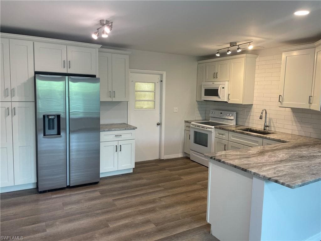Modern kitchen featuring white cabinetry, light countertops, wood-finish flooring, a subway tile backsplash, and stainless steel appliances