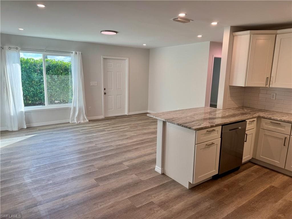 Open-concept living space with wood-finish flooring, recessed lighting, and a kitchen island featuring a stone countertop