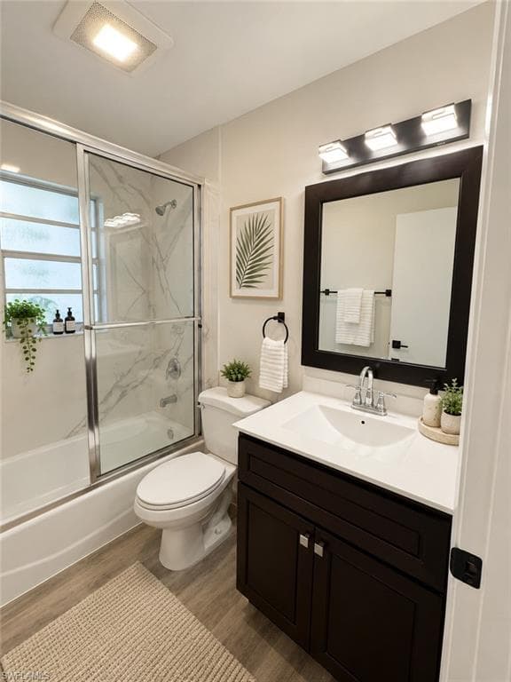 Wood-finish flooring, dark wood vanity with white countertop, chrome faucet, wall-mounted mirror, and a shower/tub combination with glass sliding doors