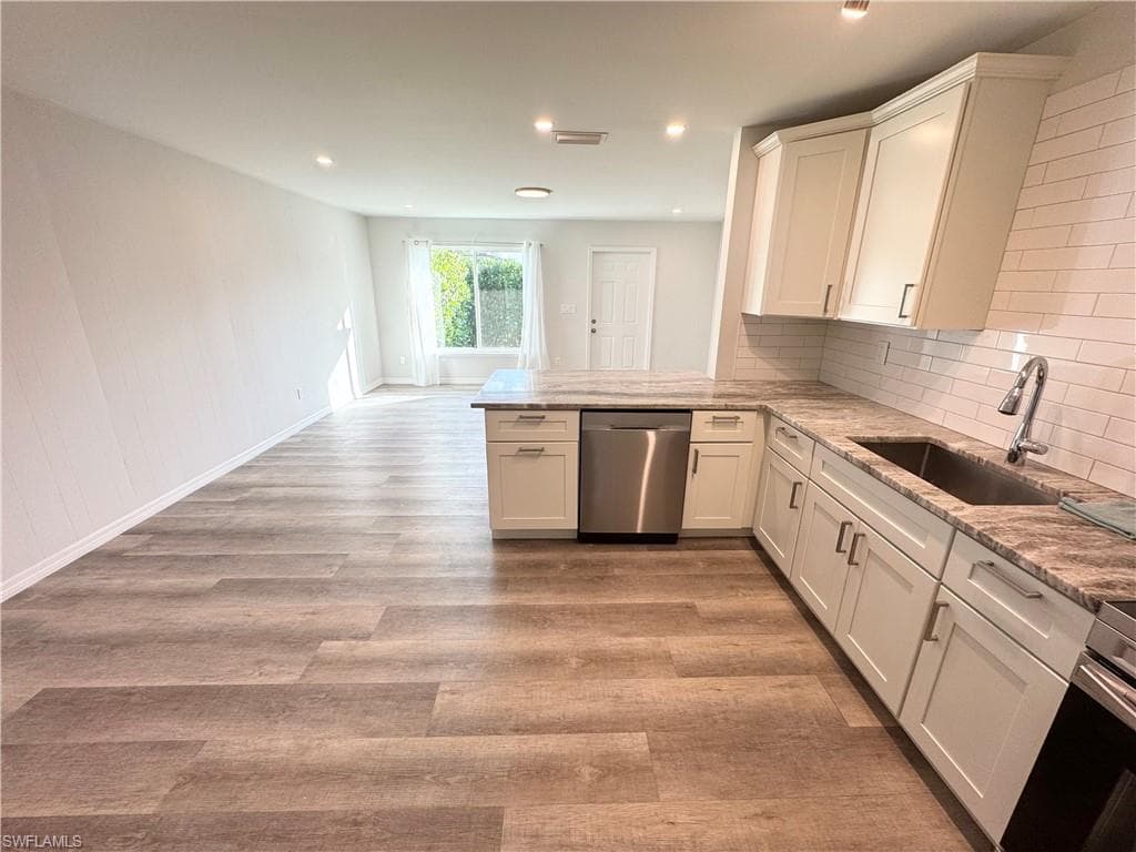 Kitchen featuring white shaker cabinetry, stainless steel dishwasher, undermount sink with gooseneck faucet, light-toned countertop, and subway tile backsplash