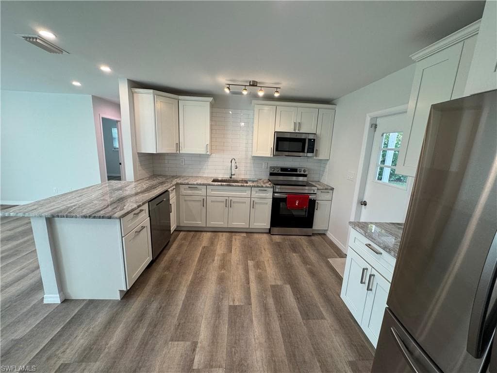 Kitchen featuring white shaker cabinetry, stainless steel appliances, wood-finish flooring, subway tile backsplash, and a large island with a countertop