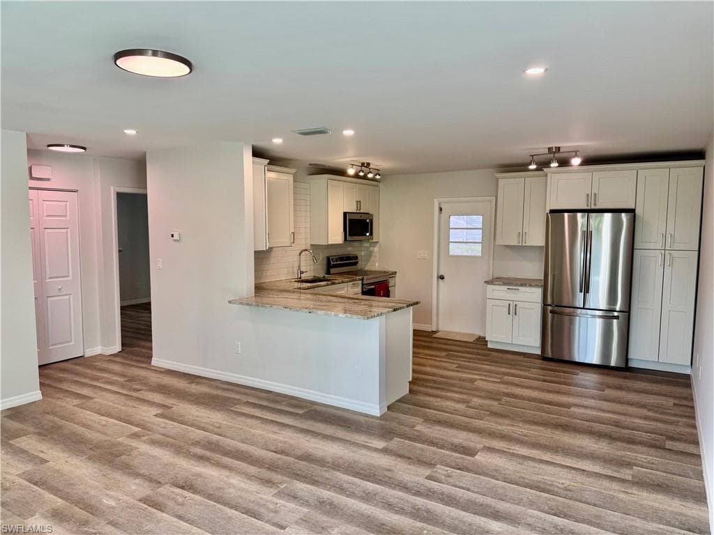 Open-concept living area with wood-finish flooring, white cabinetry, stainless steel appliances, and a breakfast bar with stone countertops