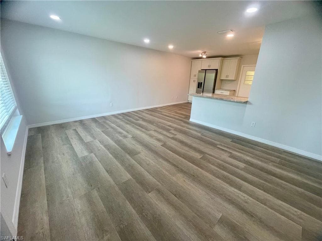 Wood-finish flooring, recessed lighting, and a kitchen featuring a breakfast bar with stone countertop, white cabinetry, and stainless steel refrigerator
