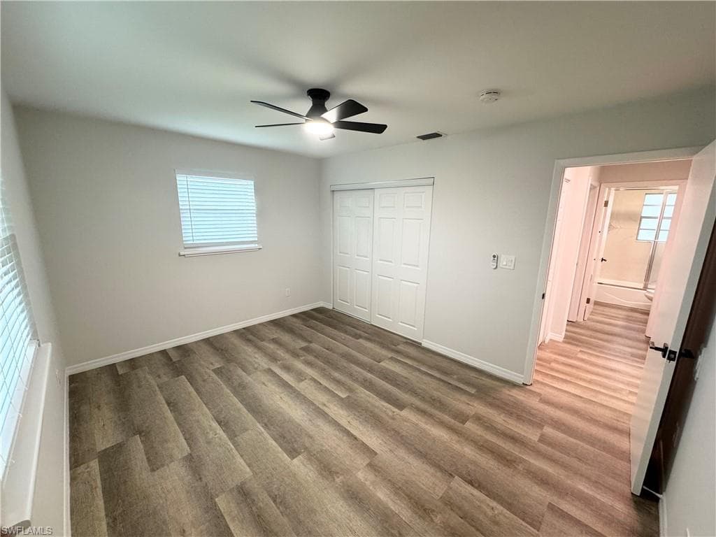Wood-finish flooring, ceiling fan with integrated lighting, window with blinds, and white bi-fold closet doors