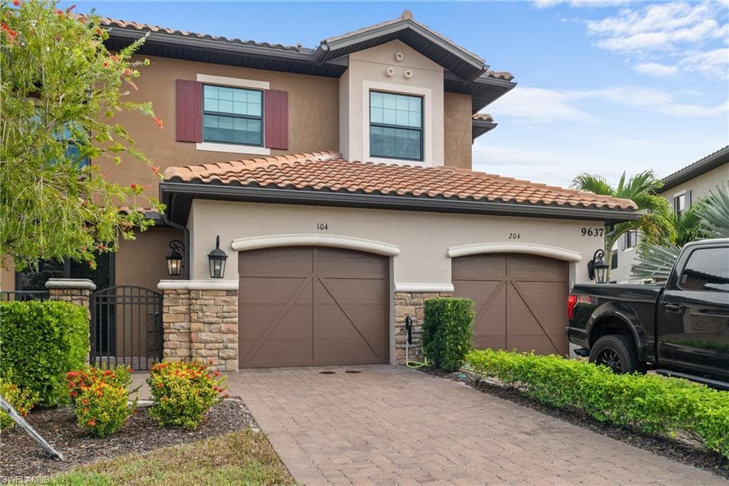 View of front facade with decorative driveway, stone siding, and stucco siding