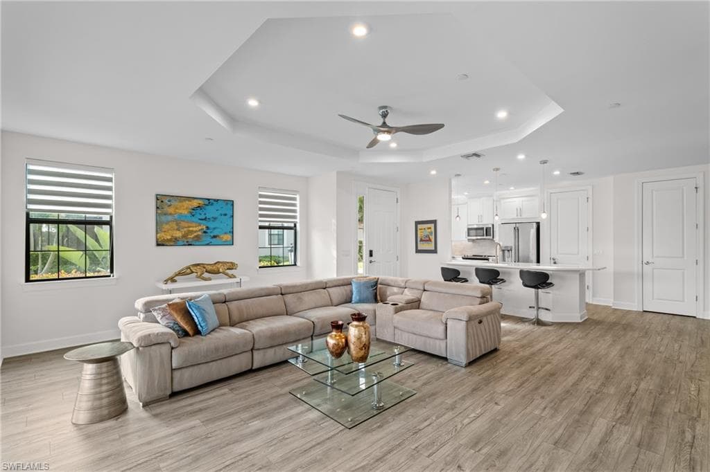 Living room featuring recessed lighting, light wood-type flooring, a ceiling fan, and a raised ceiling
