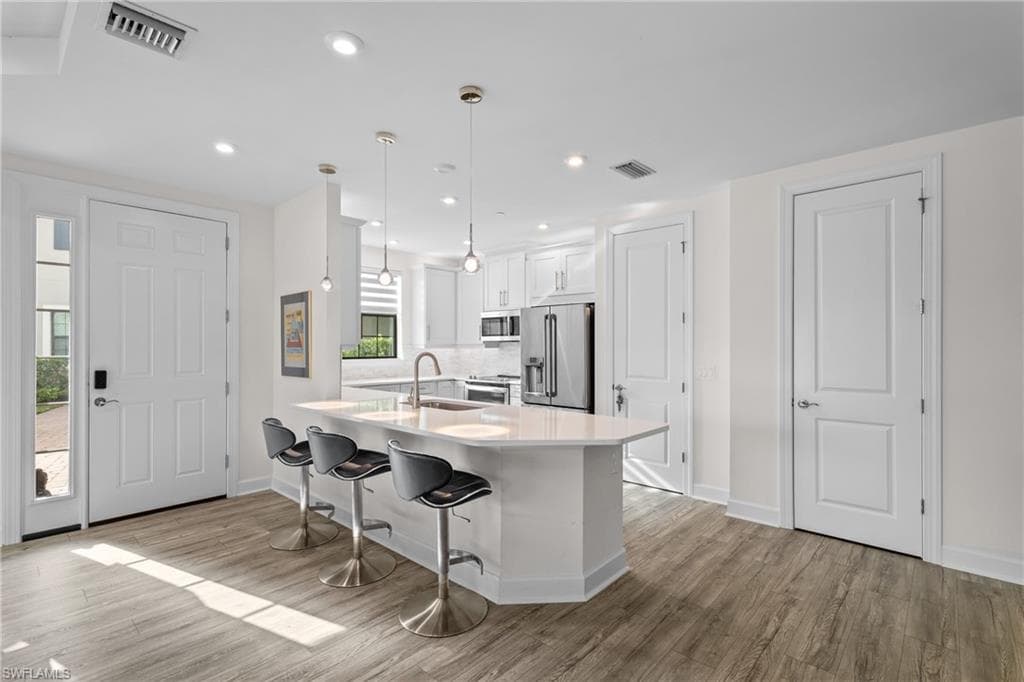 Kitchen with white cabinets, decorative light fixtures, a kitchen breakfast bar, stainless steel appliances, and a peninsula