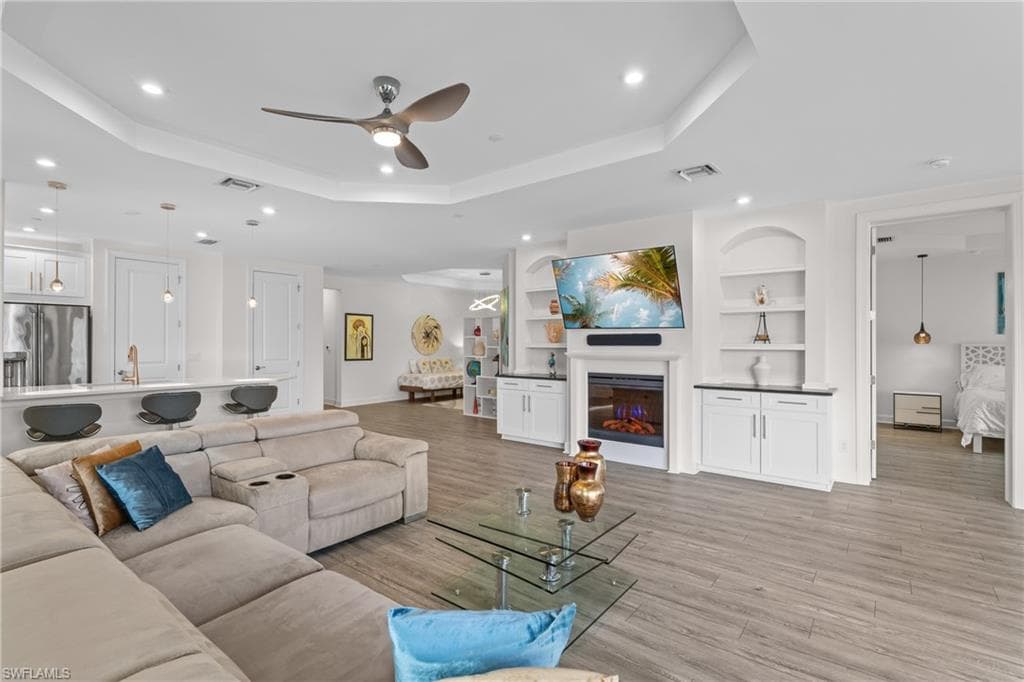 Living area featuring built in shelves, a ceiling fan, recessed lighting, a glass covered fireplace, and light wood-style flooring