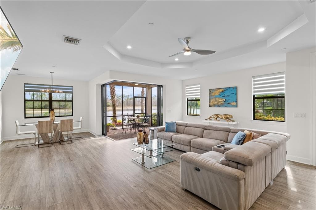 Living room featuring recessed lighting, light wood-style floors, a ceiling fan, a chandelier, and a tray ceiling