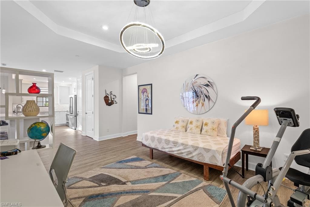 Bedroom with recessed lighting, wood finished floors, freestanding refrigerator, and a tray ceiling