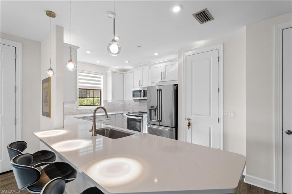 Kitchen with decorative light fixtures, stainless steel appliances, a peninsula, white cabinets, and a breakfast bar area