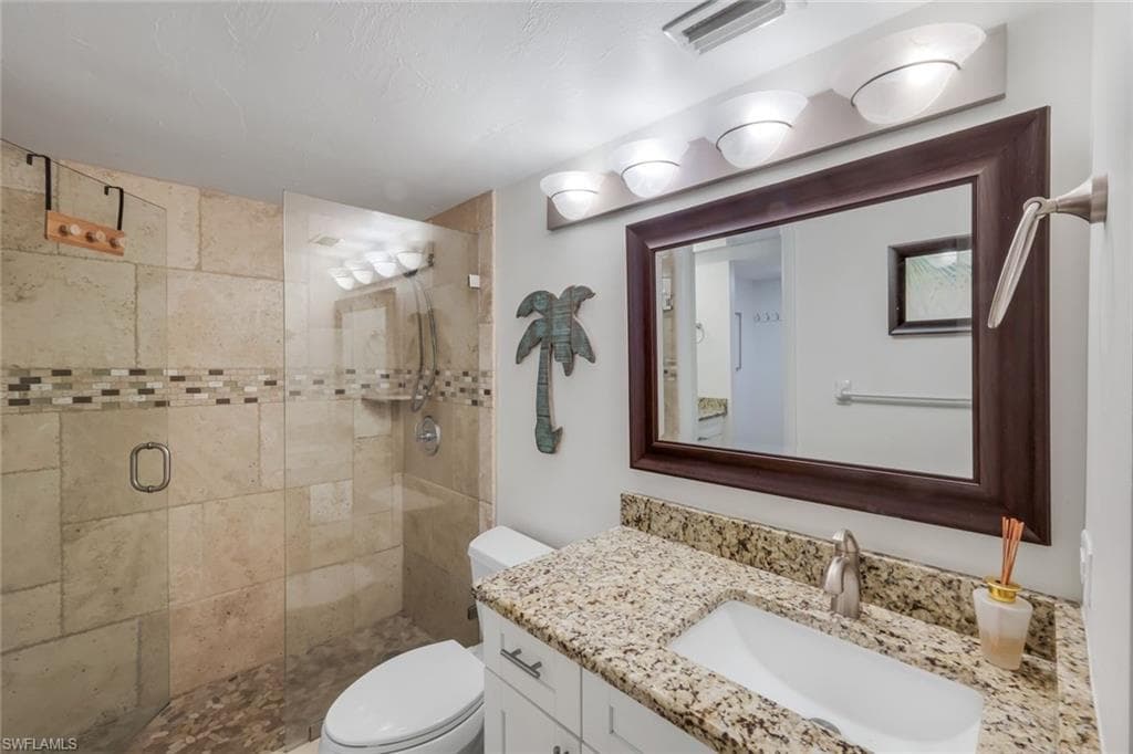 Bathroom featuring a glass-enclosed shower with stone tile walls, a decorative mosaic tile band, and a pebble-finish floor