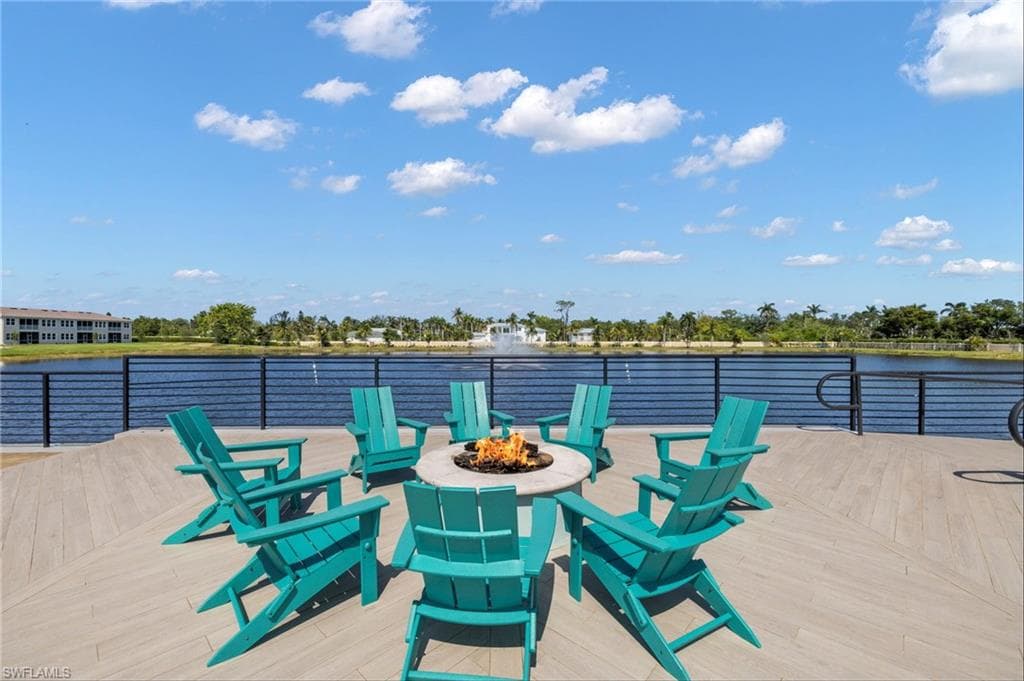 Expansive waterfront patio featuring wood-finish decking, a built-in circular fire pit, and a black horizontal bar railing