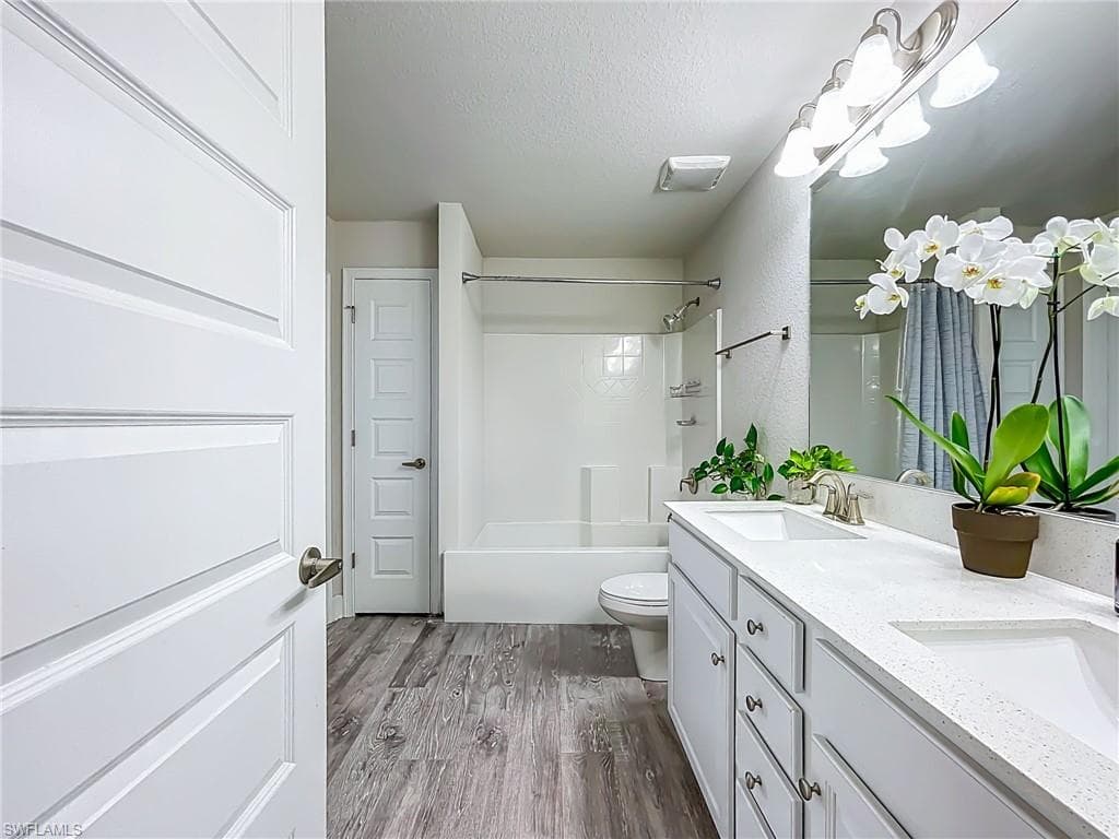 Full bath featuring double vanity, shower combination, wood finished floors, and a textured ceiling