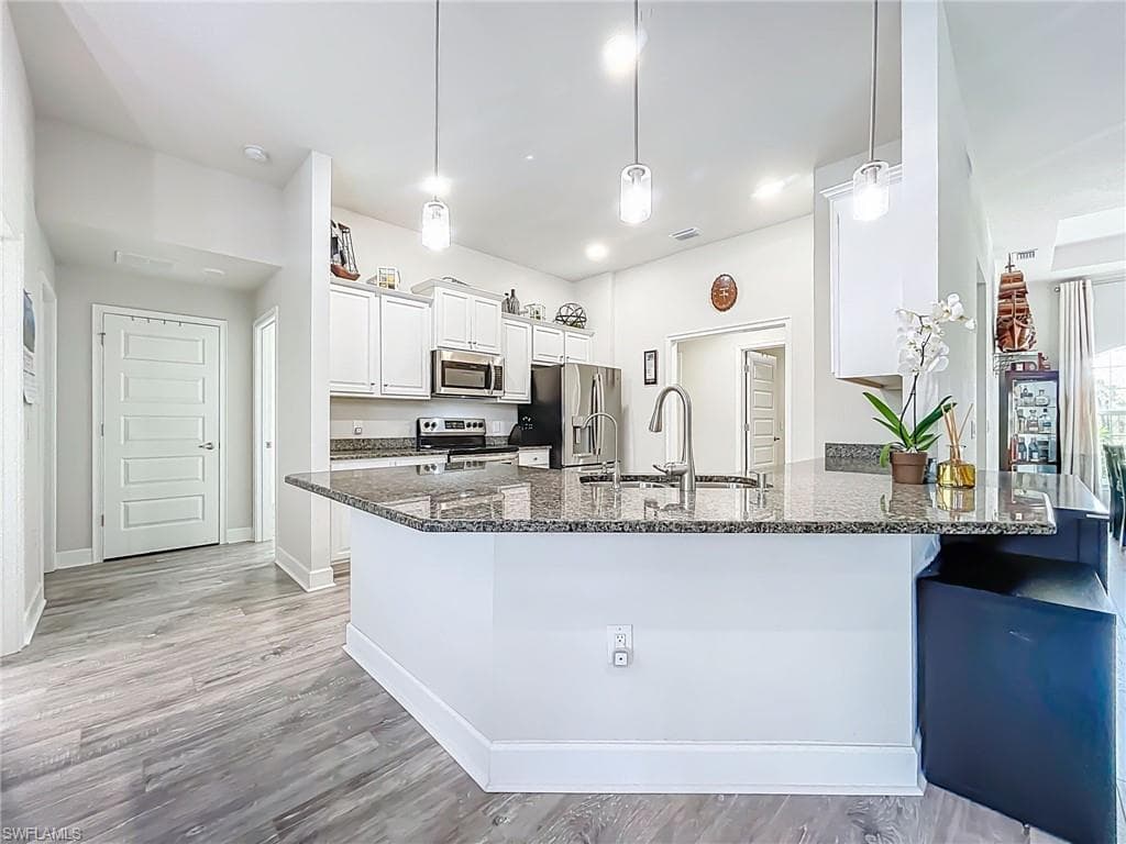 Kitchen featuring appliances with stainless steel finishes, a peninsula, dark stone counters, white cabinetry, and a kitchen breakfast bar