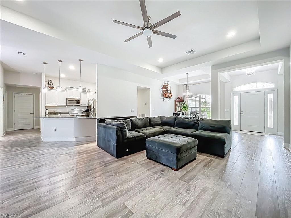 Living room featuring a chandelier, light wood finished floors, ceiling fan, a tray ceiling, and recessed lighting