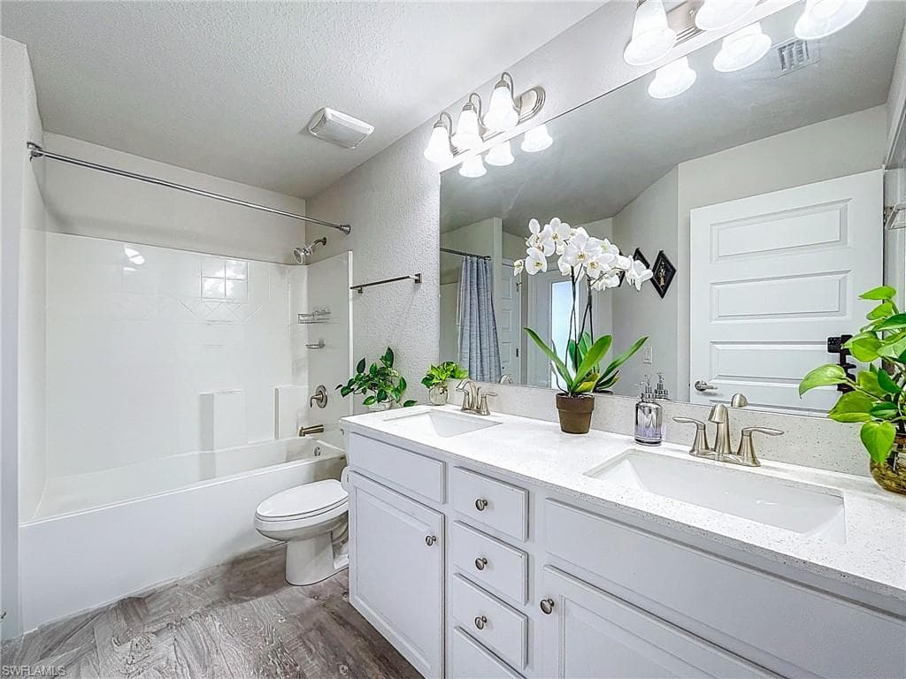 Bathroom featuring double vanity, shower / bath combo with shower curtain, wood finished floors, and a textured ceiling