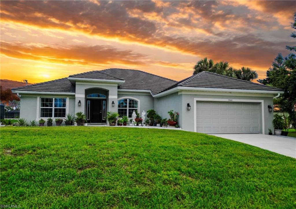 Single story home featuring stucco siding, a lawn, an attached garage, and concrete driveway