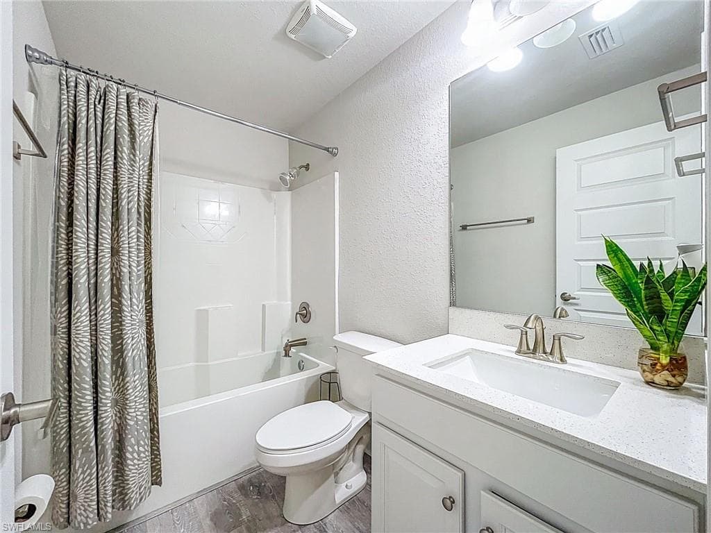 Full bath with wood finished floors, a textured wall, shower / tub combo, and vanity
