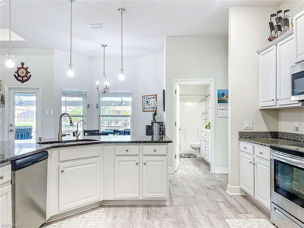 Kitchen featuring stainless steel appliances, light wood-style flooring, white cabinetry, dark stone countertops, and a chandelier