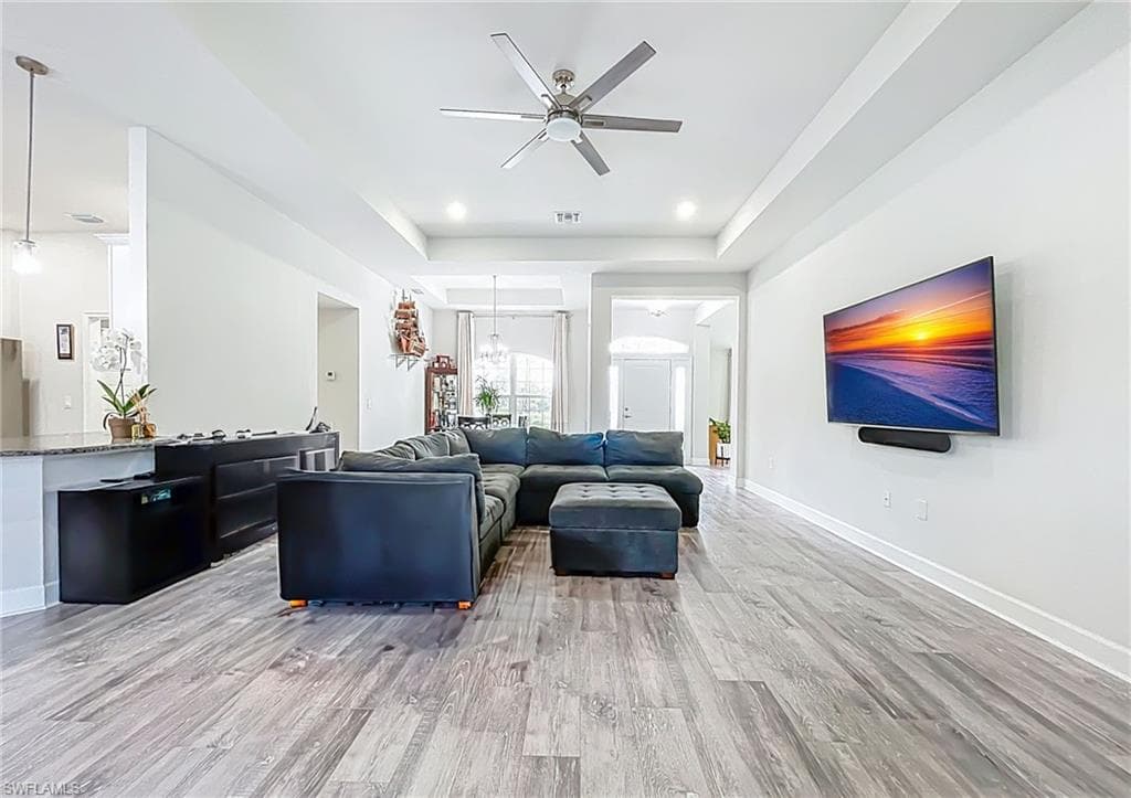 Living area with a ceiling fan, light wood-style floors, and a raised ceiling
