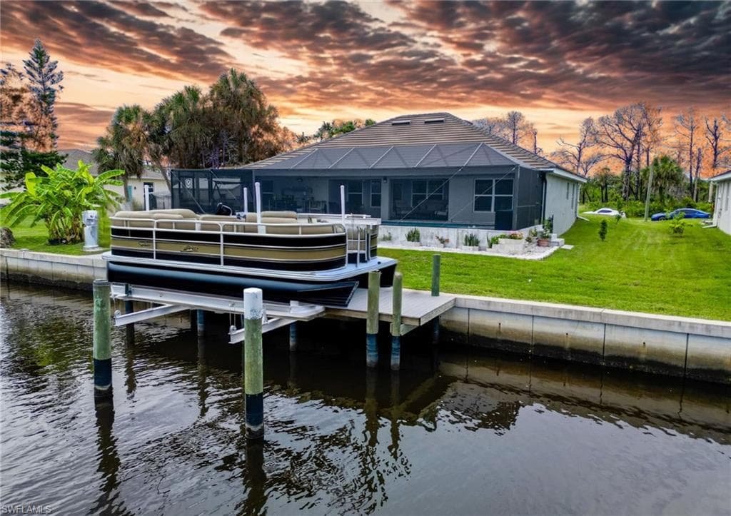 Dock with boat lift, a water view, a lanai, and a lawn