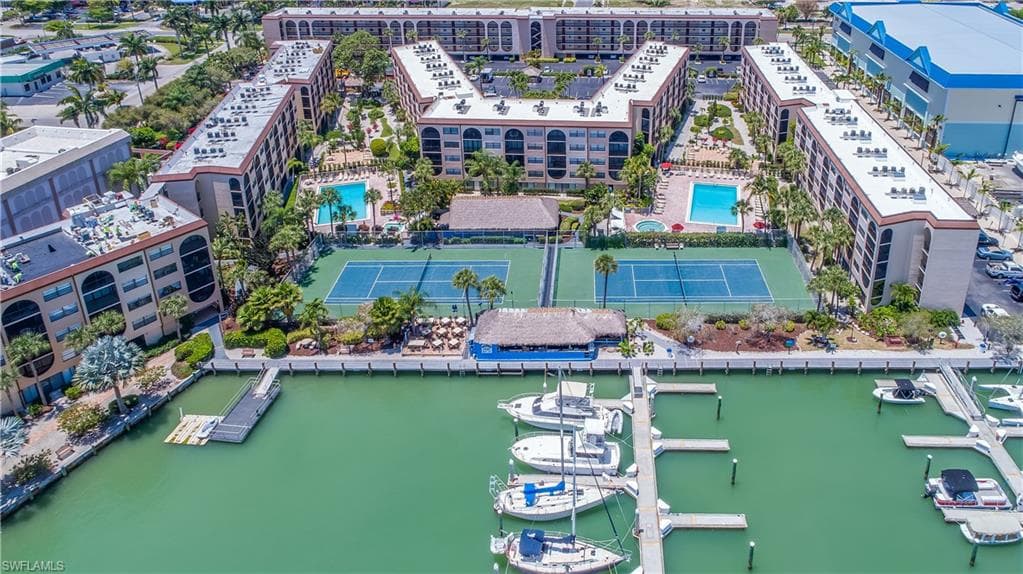 Waterfront condominium complex featuring a private marina with multiple boat slips, two outdoor swimming pools, and two tennis courts