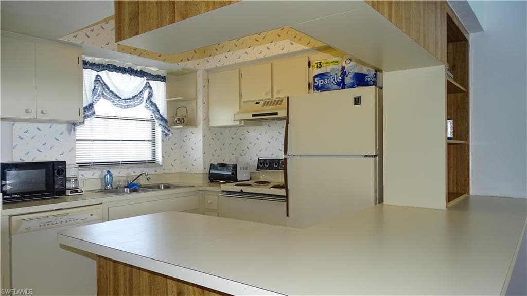 Kitchen featuring a peninsula countertop, white appliances, and ample cabinetry