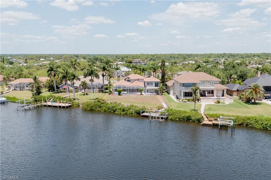 Waterfront property featuring multiple boat docks, mature palm trees, expansive rear patio