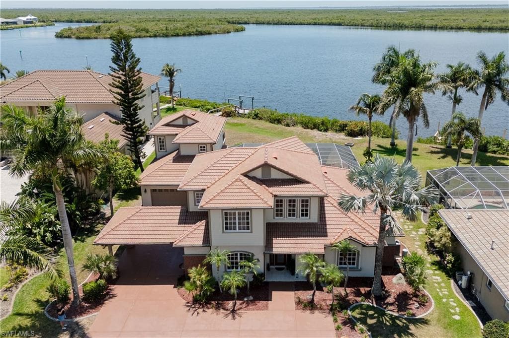 Waterfront residence featuring a tiled roof, multi-story architecture, attached garage, covered carport, and mature tropical landscaping