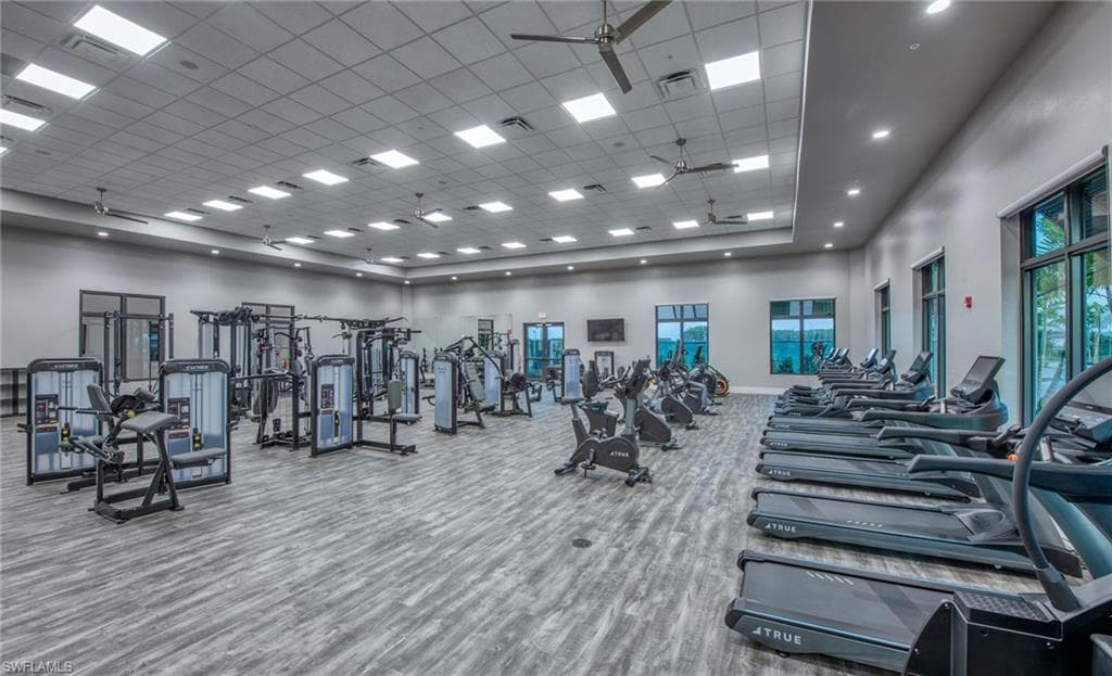 Spacious fitness center featuring a variety of cardio and strength training equipment, recessed lighting, ceiling fans, large windows, and wood-finish flooring