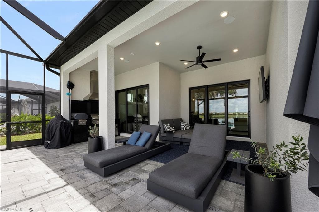 Screened patio featuring paver flooring, an outdoor kitchen with an integrated range hood, a ceiling fan, recessed lighting, and sliding glass doors