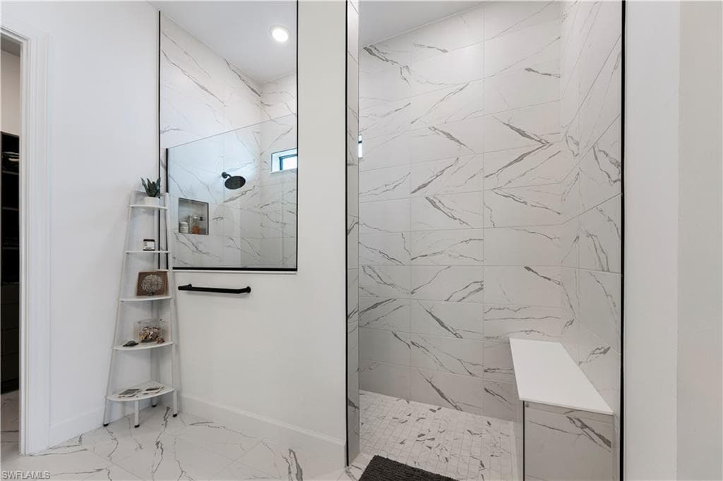 Walk-in shower featuring large-format tile with grey veining, a built-in shower niche, a fixed rainfall shower head, and a built-in bench