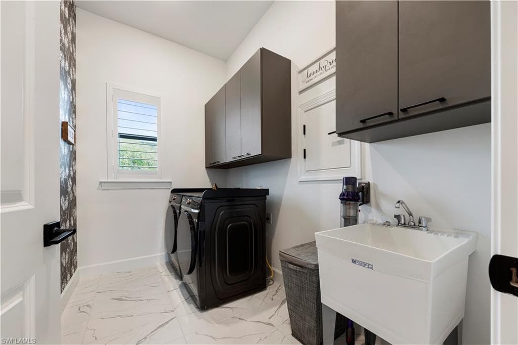 Dedicated laundry area featuring modern appliances, white marble-look tile flooring, and dark cabinetry